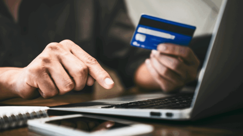 A person is holding a debit card to make a purchase online during Cyber Monday.