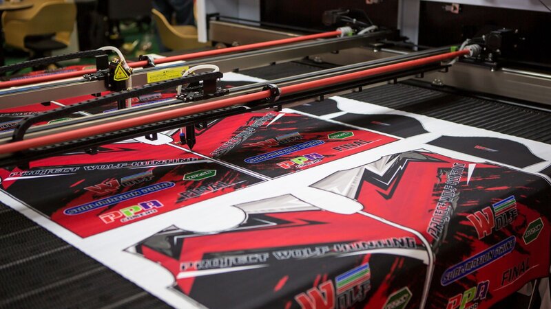 A printing machine applying vibrant designs on fabric, featuring bold red and black colors with various logos and text.