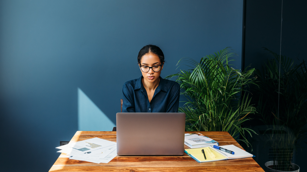 A woman sitting in front of a laptop with a dark blue background.