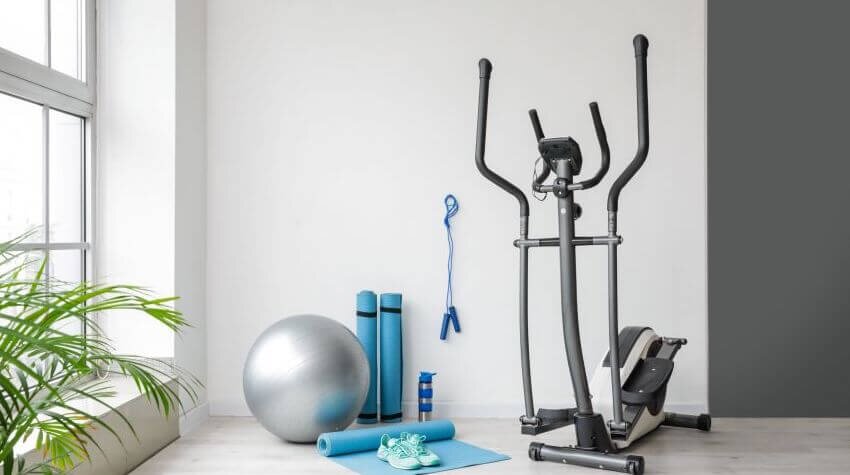 A home gym set with an elliptical, yoga mat, jumping rope, and yoga ball.
