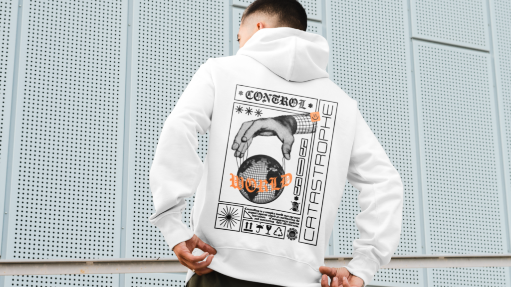 A man in a white hoodie with futuristic graphic designs on the back stands against a perforated metal wall.