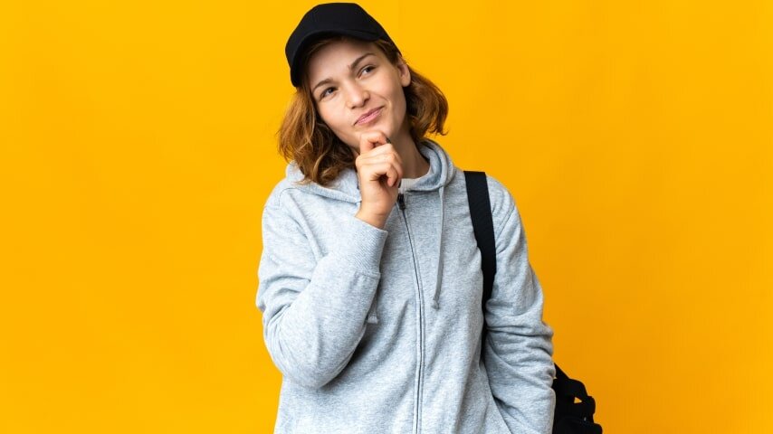 Woman wearing a black baseball hat and looking thoughtful.