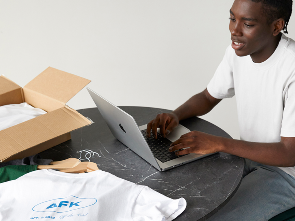 A man using a laptop on top of a marble table, with a white t-shirt on the corner of the table.