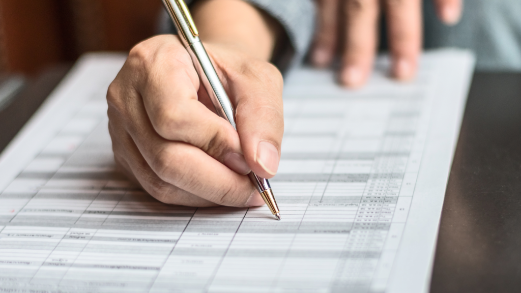 A man's hand holding a pen, writing on a sheet of paper.