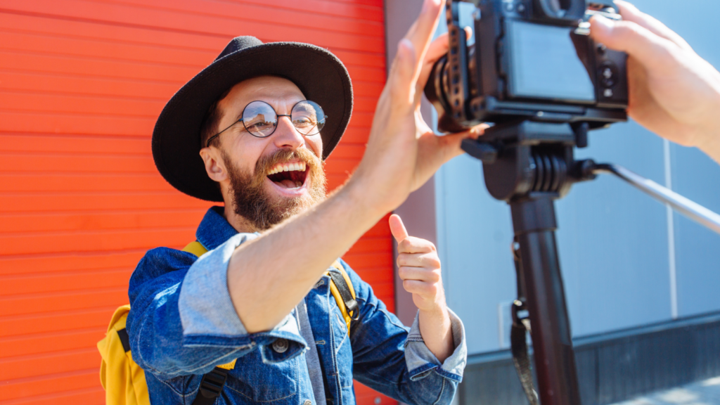A man wearing a hat smiles as he films a video of himself, capturing a moment of joy and self-expression.