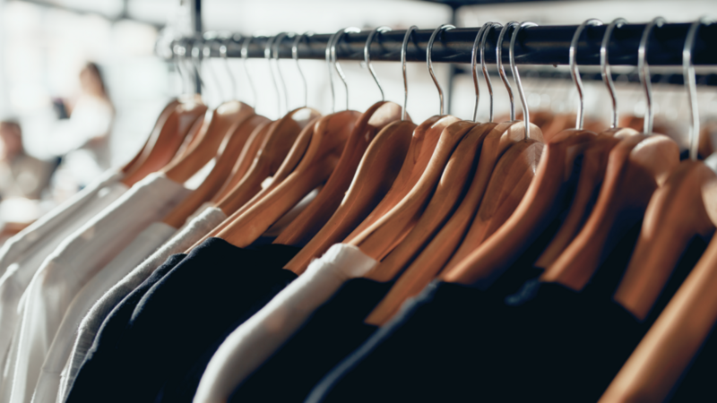 Clothes of various styles and colors hanging on hangers in a well-organized clothing store.