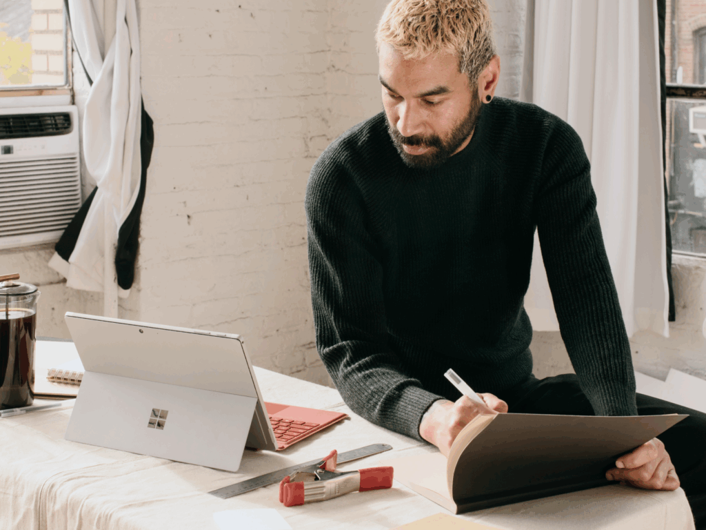 A young bearded man is making notes from a laptop on “How to make prints of your art”.