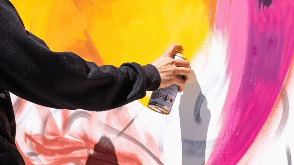 A person spray paints a wall, creating vibrant colors and patterns.