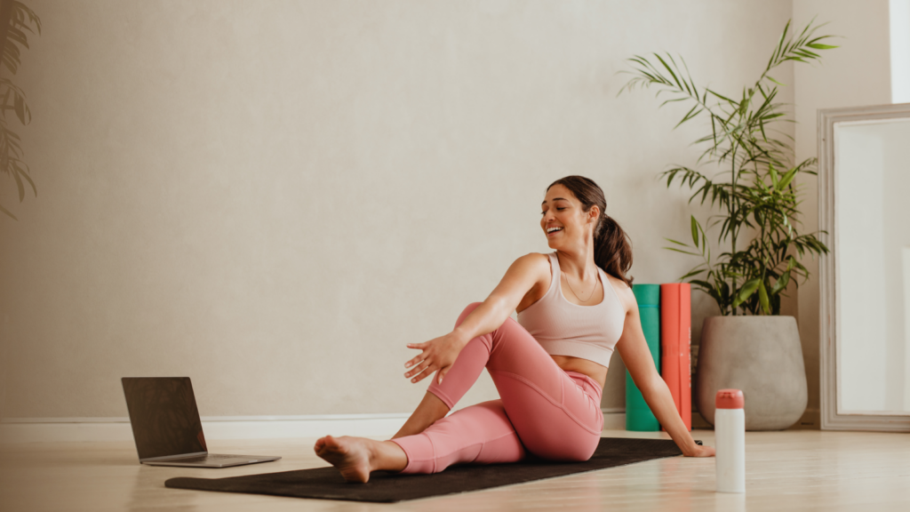 A woman on a yoga mat uses her laptop, illustrating the balance between mindfulness and professional tasks while doing an online fitness class.