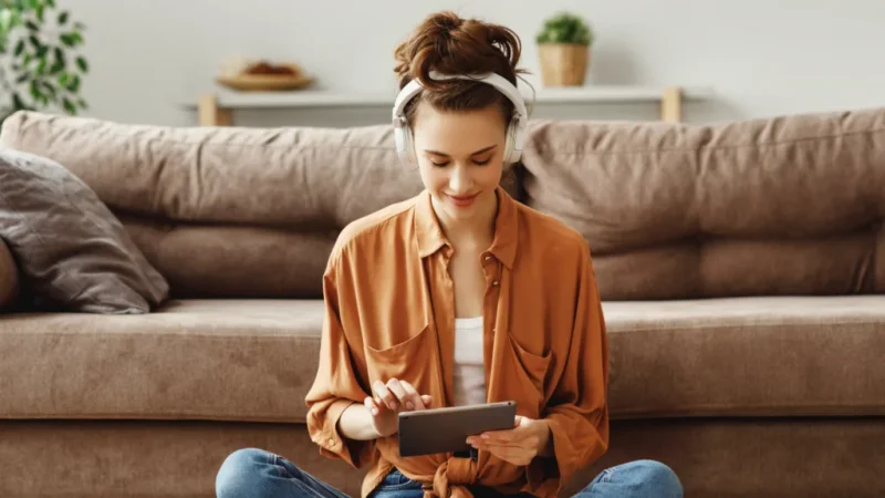 A woman sitting on the floor, focused on using a tablet in a casual indoor setting.