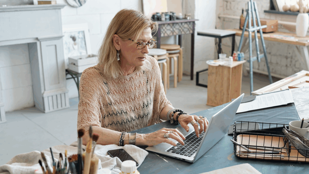 An older woman is using a laptop in an art studio.
