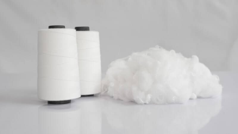 Two spools of polyester thread next to a clump or polyester fiber.