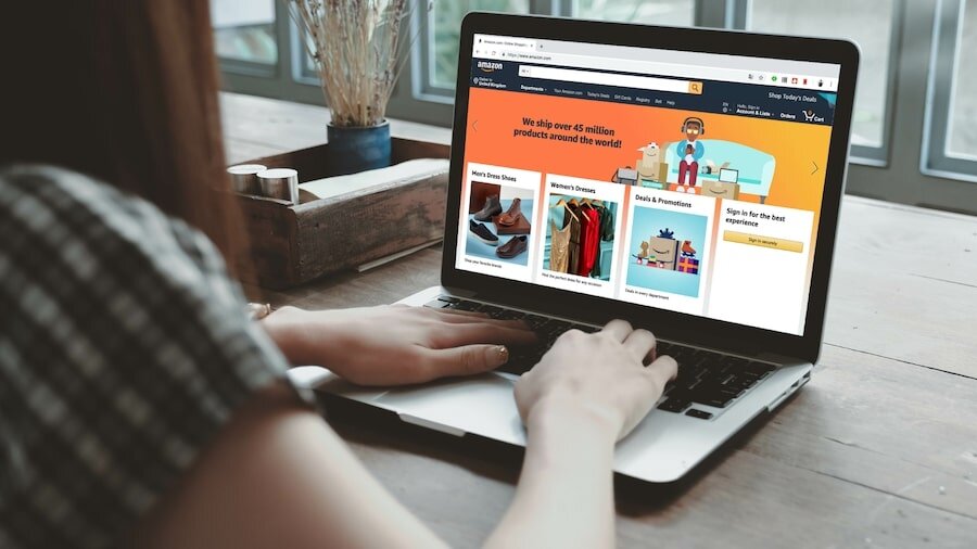 A laptop with a woman’s hand on the keyboard and the Amazon homepage on the screen.