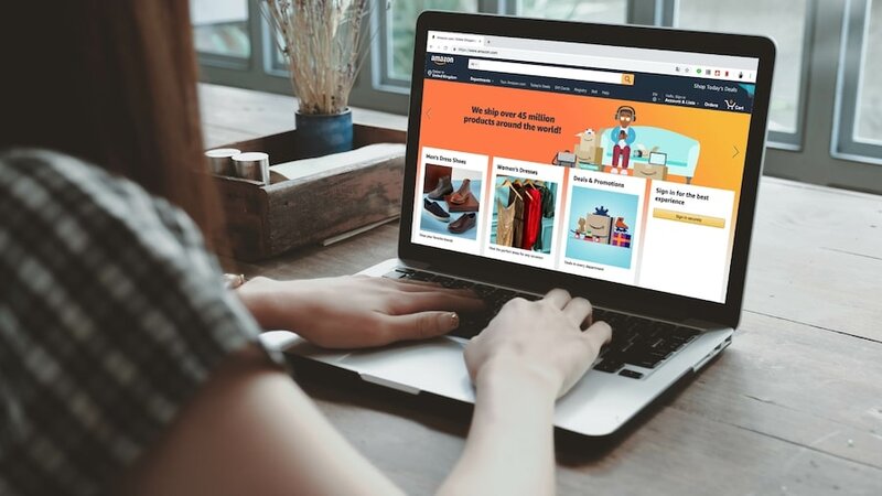 A laptop with a woman’s hand on the keyboard and the Amazon homepage on the screen.