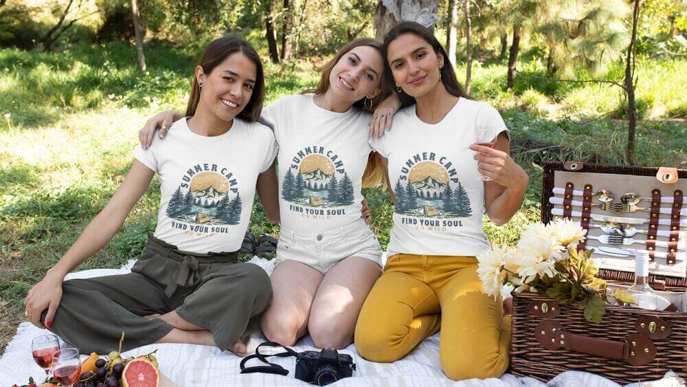 Three women wearing custom white Gildan GIL4100 t-shirts with a summer camp illustration.