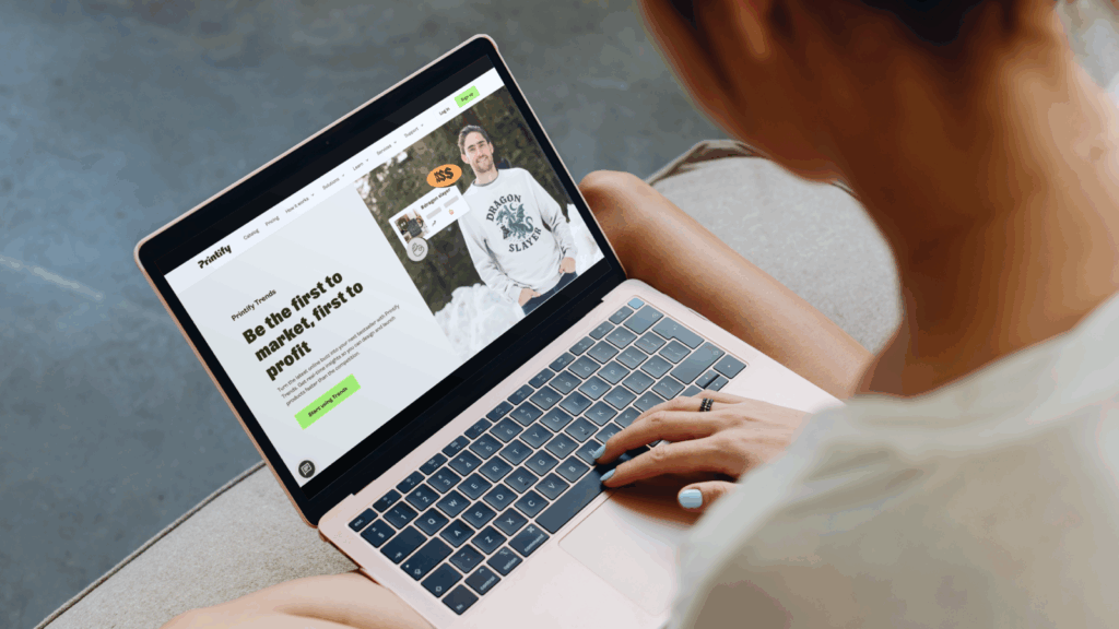 A woman using a laptop displaying the Printify Trends website.