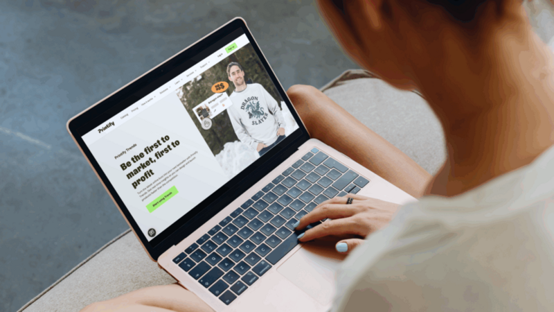 A woman using a laptop displaying the Printify Trends website.