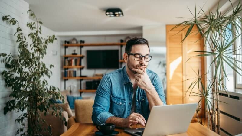 A man sitting at his desk and looking thoughtfully at his laptop.