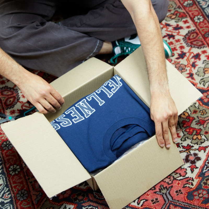 A man is unpacking a delivery box with a blue “Wellness” t-shirt.