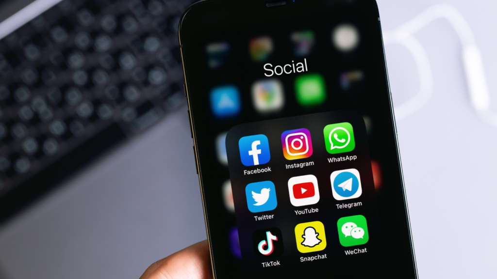 A person holding a smartphone displaying various social media applications on the screen.