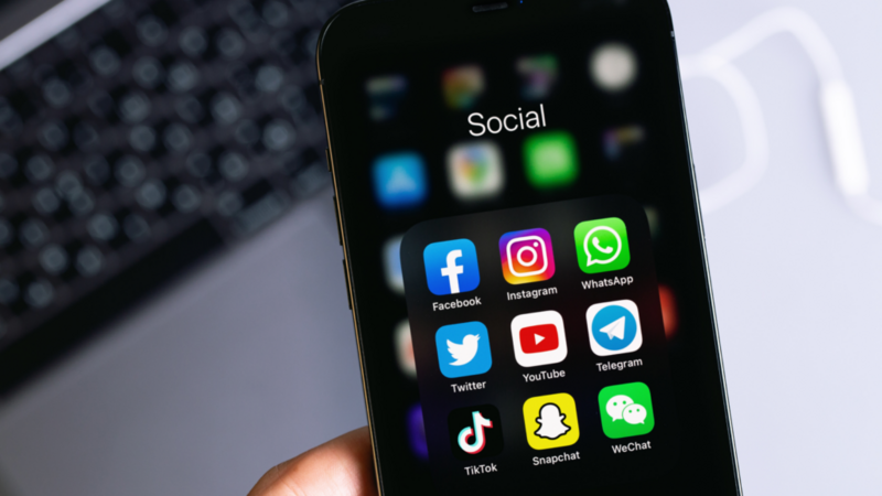 A person holding a smartphone displaying various social media applications on the screen.