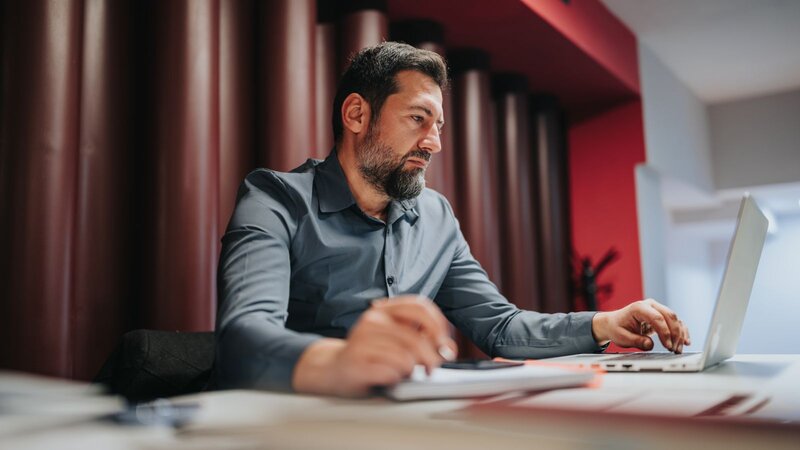 A man with a beard working on a laptop while sitting at a desk, searching for how to get free print designs.