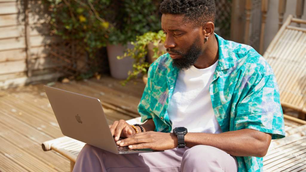 A man sitting outside with a laptop on his lap, searching for what is a tariff.