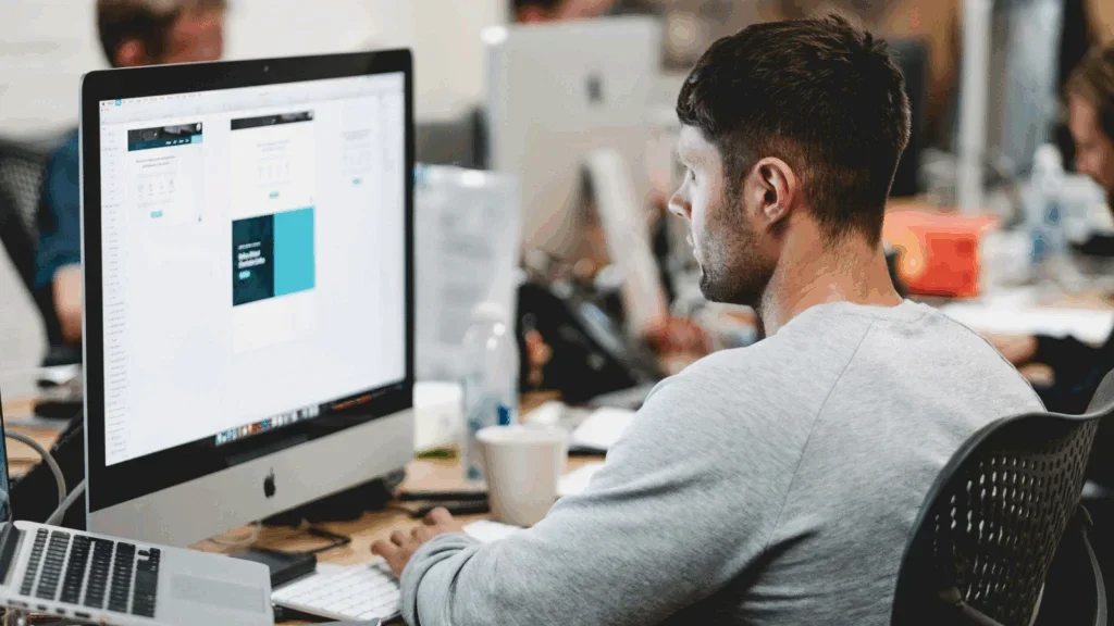 A man is doing graphic design work on a large monitor.