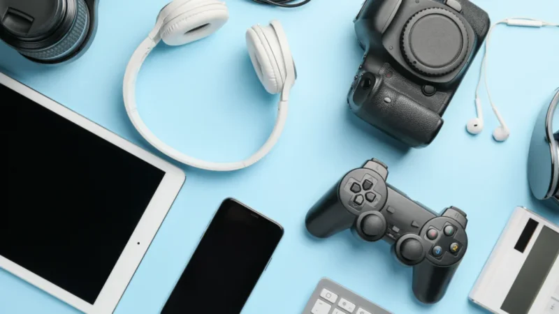 Various electronics (tablet, mobile phone, DSLR camera, and lens, gamepad, headphones) on a blue background.