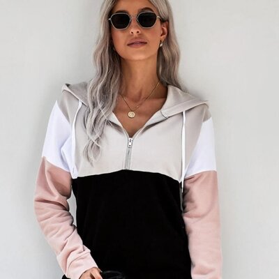A woman wearing shades and a hoodie that has a color-block design in black, beige, white, and pink.