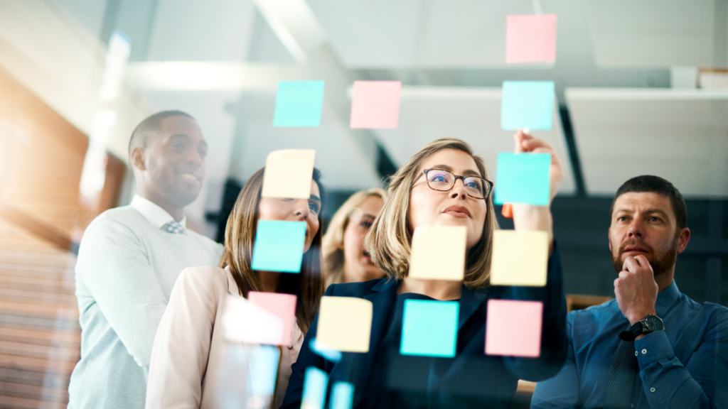 Several people stand near a glass wall adorned with sticky notes, collaborating and sharing ideas in a creative environment.