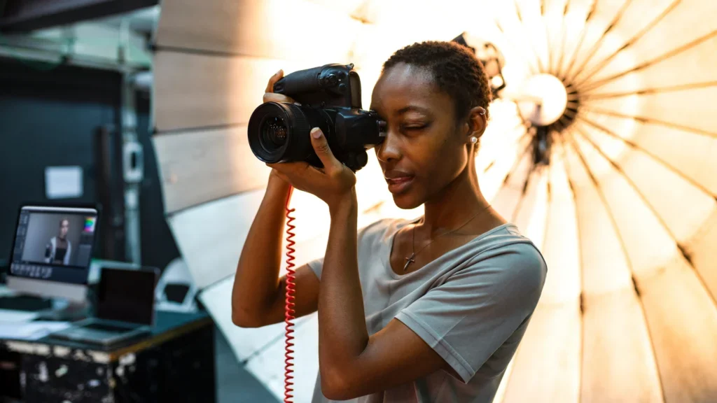A woman holds a camera in front of a bright light, poised to take a photograph, showcasing her passion for photography.