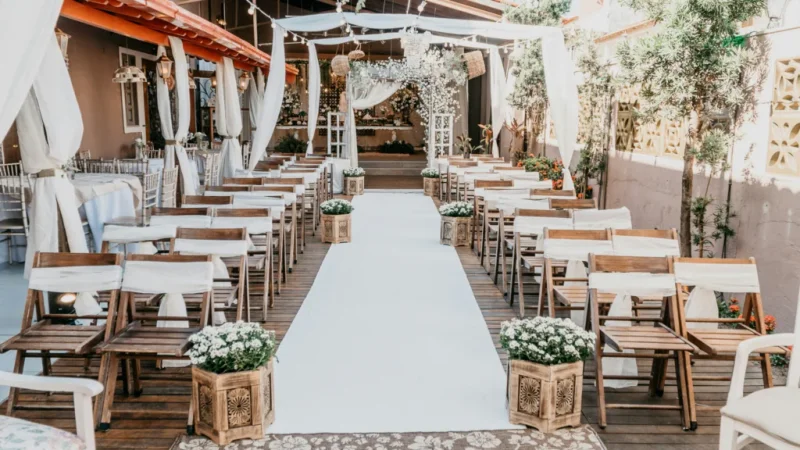 An outdoor wedding ceremony featuring wooden chairs arranged with white flowers adorning the aisle.