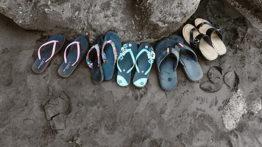 Multiple pairs of flip-flops on a beach.