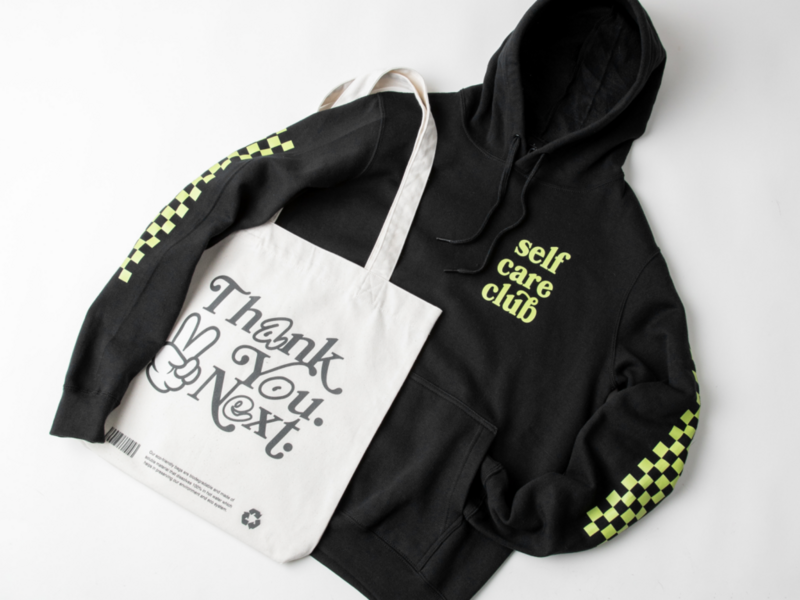 A custom black “Self-care club” hoodie next to a “Thank you. Next.” tote bag.