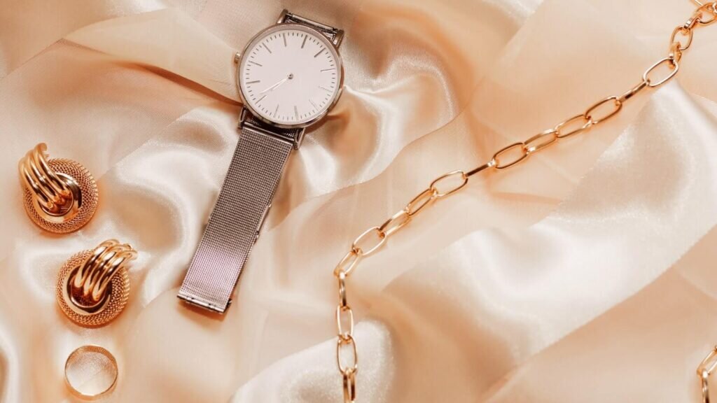 Elegant jewelry and a watch placed on a beige fabric.