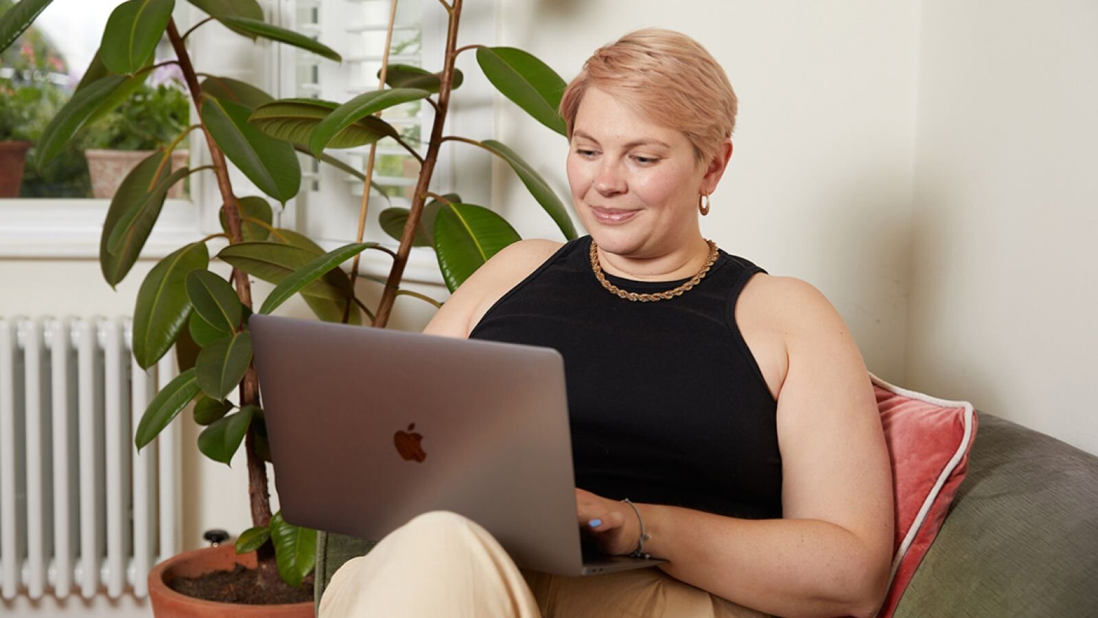 A young, smiling woman in a black shirt sits in a large chair, using a laptop to learn how to create a text design.