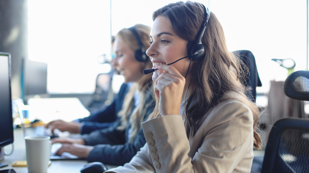 A woman wearing a headset, focused on her work, seated at a desk in a modern office environment.