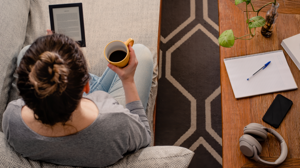 A woman using a tablet and sipping from a coffee mug, seated comfortably at a table.