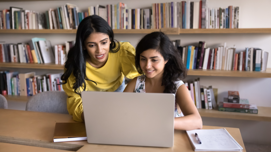 Two women engaged in discussion while examining information in a laptop.