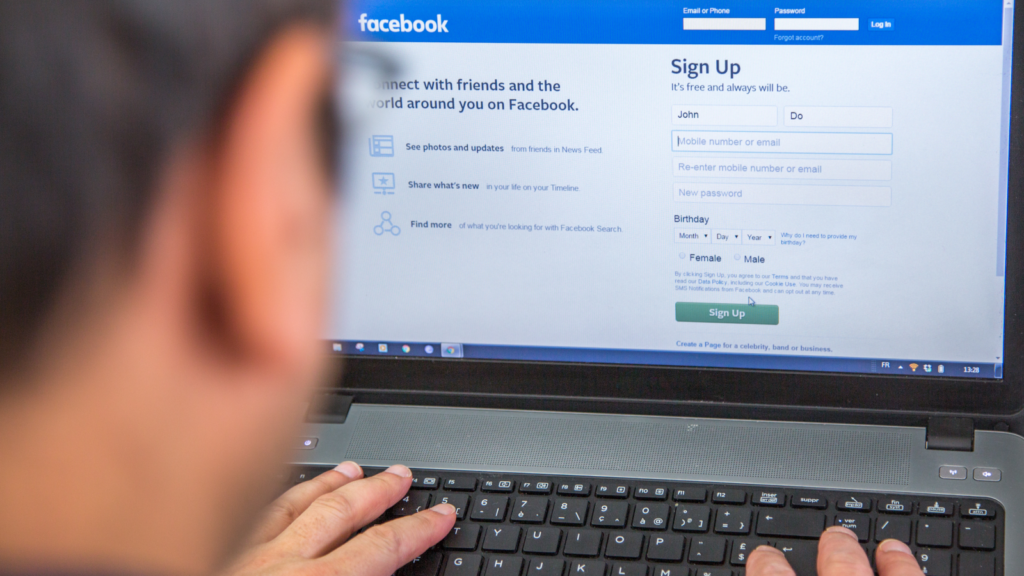 A blurred person in front of a laptop with Facebook’s sign up page on the screen.