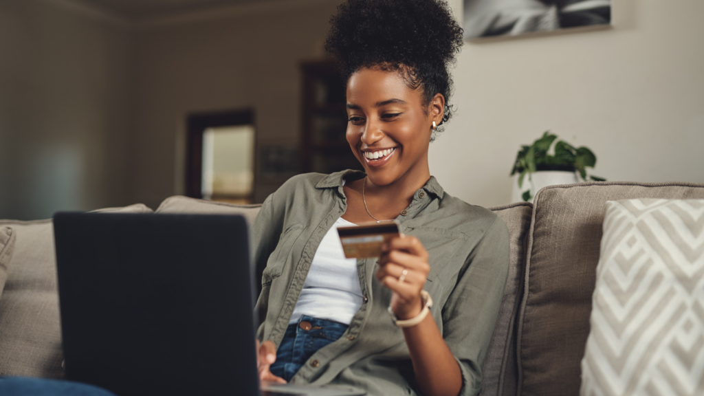 A woman sitting at a table, using her laptop and holding a credit card to shop for groceries online.