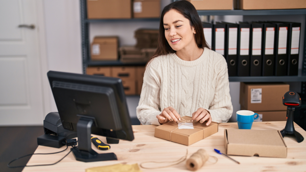 A woman sitting at a desk, looking at a monitor and decorating a delivery package.