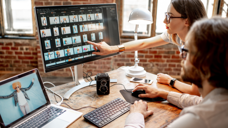 A woman and a man review photos on a computer in a brick-walled office.
