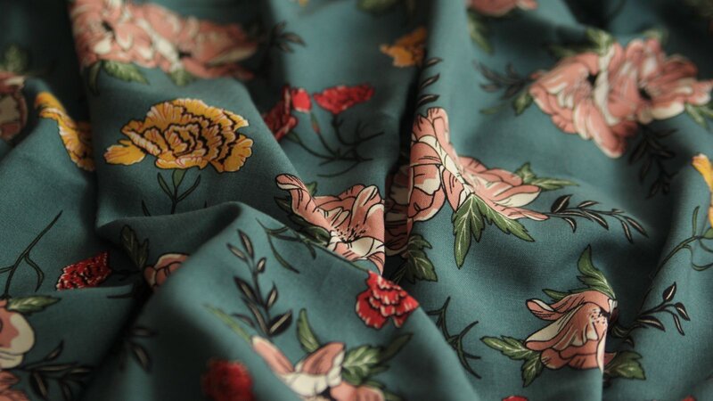 Close-up of teal fabric featuring a floral pattern with pink, yellow, and red flowers on a smooth surface.
