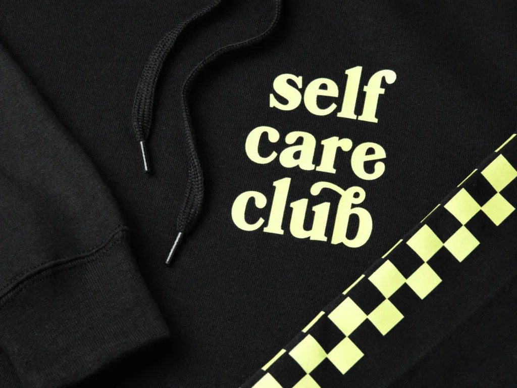 A black “Self-care club” hoodie close-up shot.
