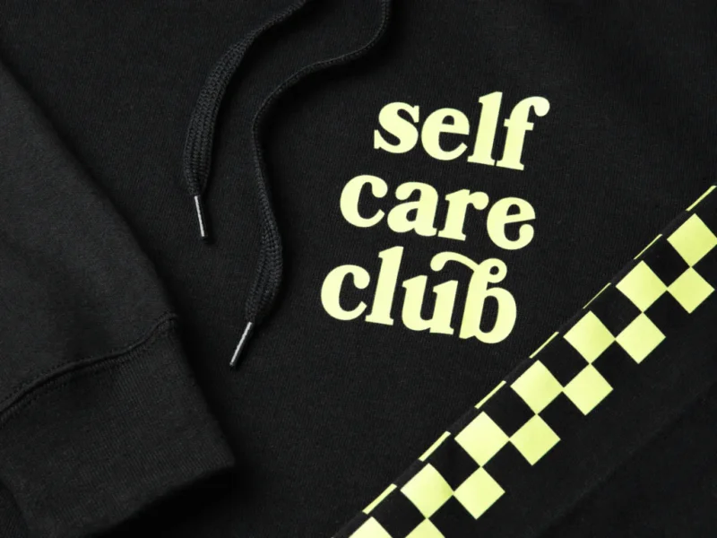 A black “Self-care club” hoodie close-up shot.
