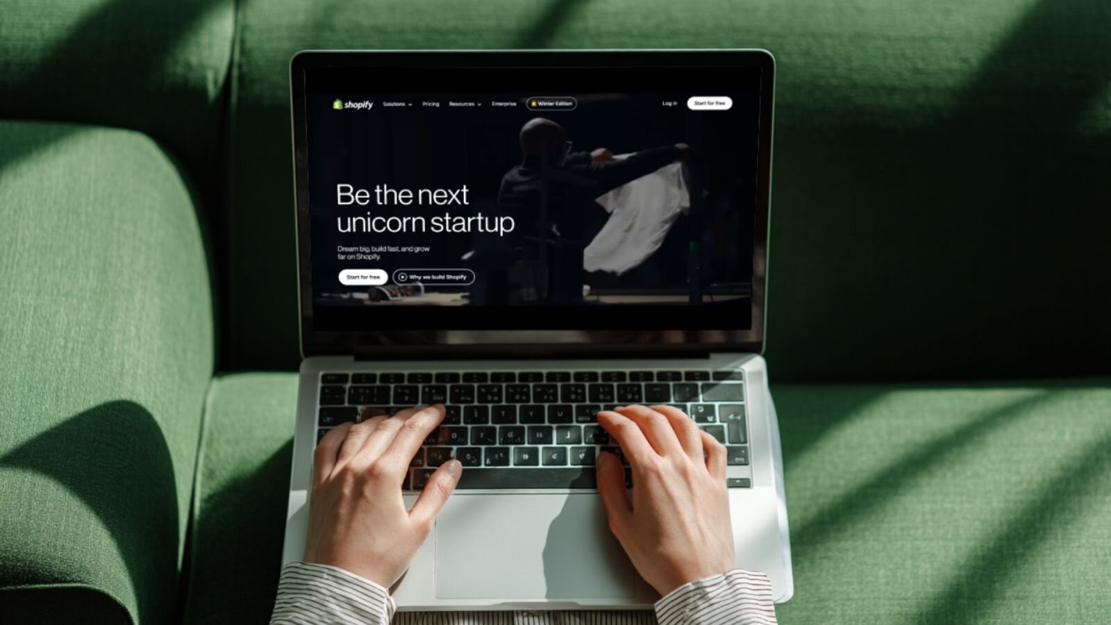 A person is using a laptop with Shopify’s homepage displayed.