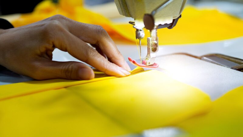 A close-up of a hand guiding yellow fabric under a sewing machine needle, showcasing the sewing process.