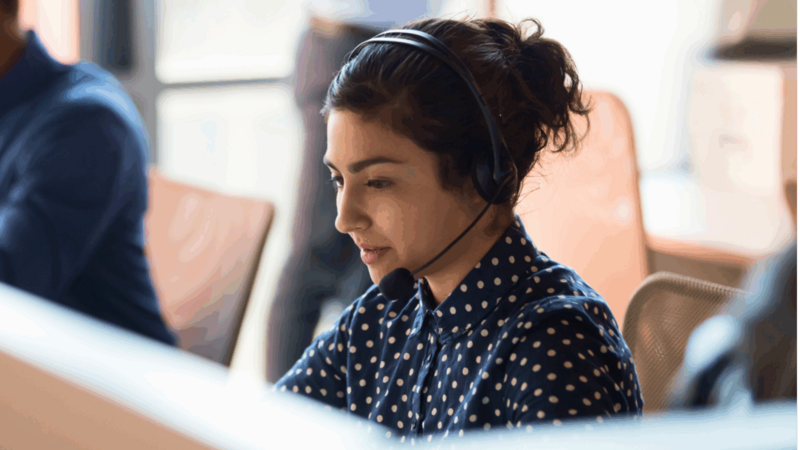 A woman wearing a headset, focused on her work in a modern office environment.